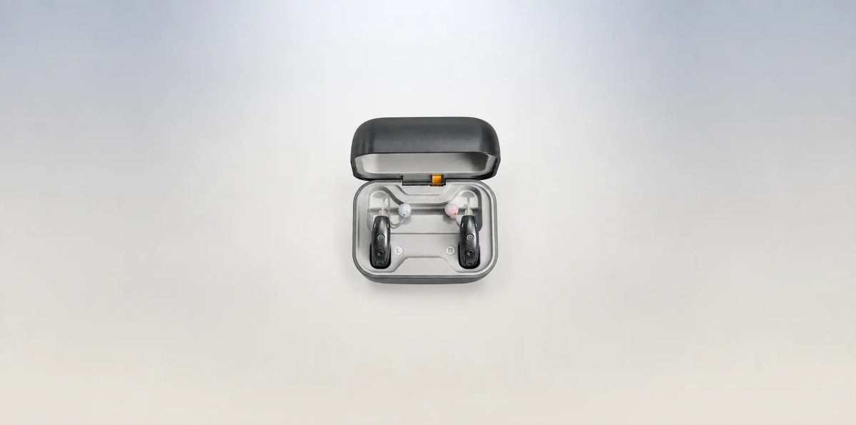 Wide-angle shot of grey AuyeeSnc OmniTouch hearing aids seated inside their open charging case